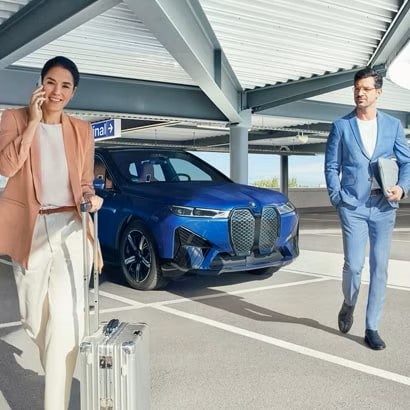 A couple in business attire walk away from a BMW sedan in a parking garage